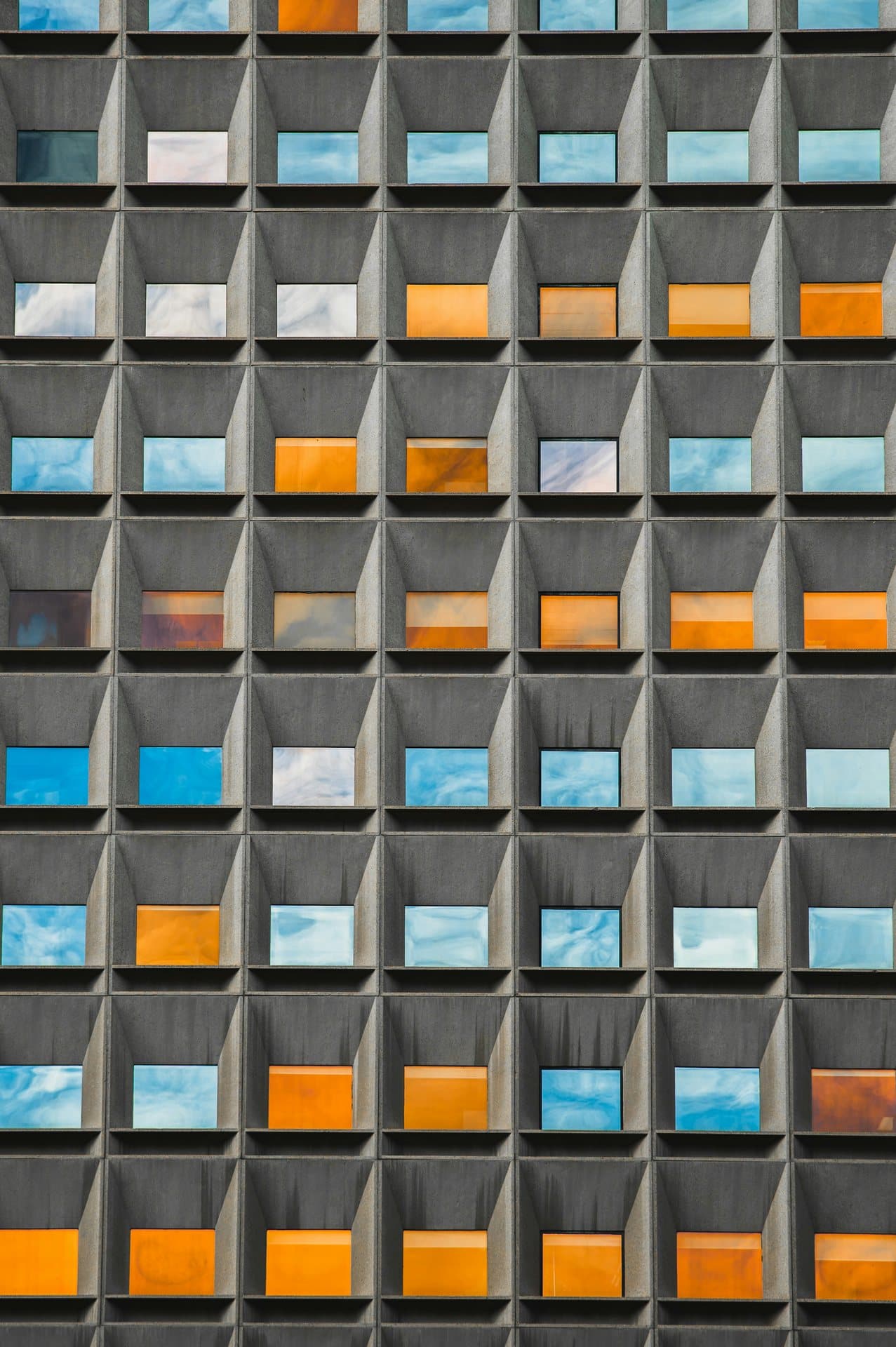 Grid of windows on a concrete brutalist facade, blue and amber glass